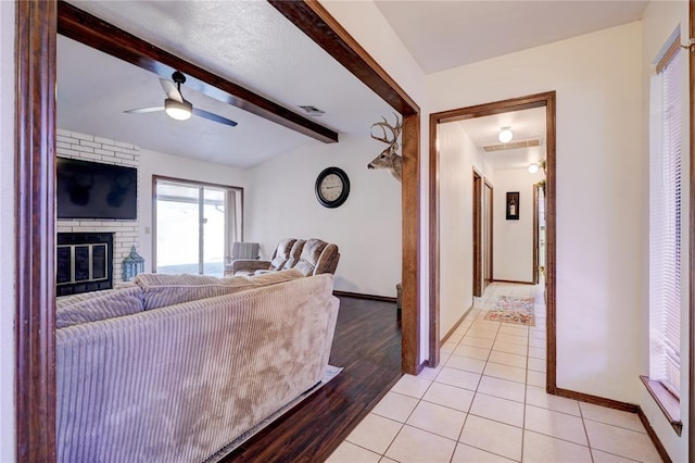 living room with light tile patterned floors, lofted ceiling with beams, a fireplace, a ceiling fan, and baseboards