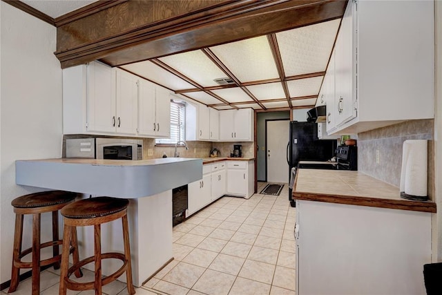 kitchen featuring visible vents, a breakfast bar area, a peninsula, white cabinetry, and backsplash