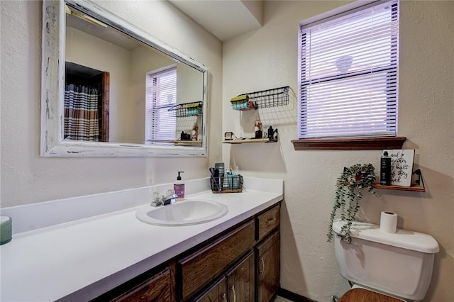 full bath featuring toilet, a textured wall, and vanity