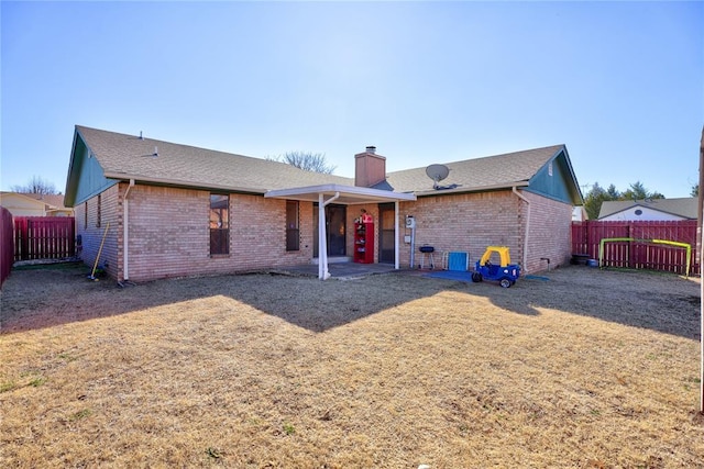 rear view of property with a fenced backyard, a chimney, a lawn, and brick siding