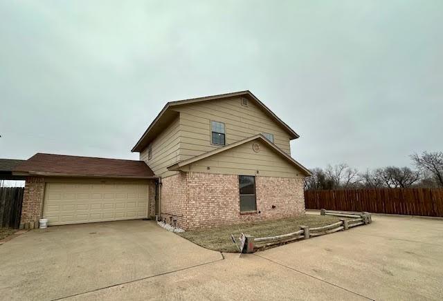 view of home's exterior featuring concrete driveway, brick siding, fence, and an attached garage