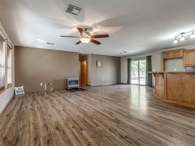 unfurnished living room featuring a ceiling fan, wood finished floors, visible vents, and heating unit