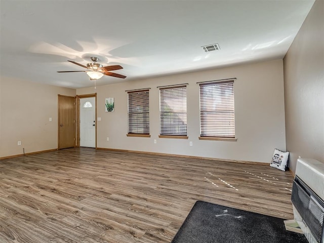 unfurnished living room featuring heating unit, visible vents, ceiling fan, wood finished floors, and baseboards