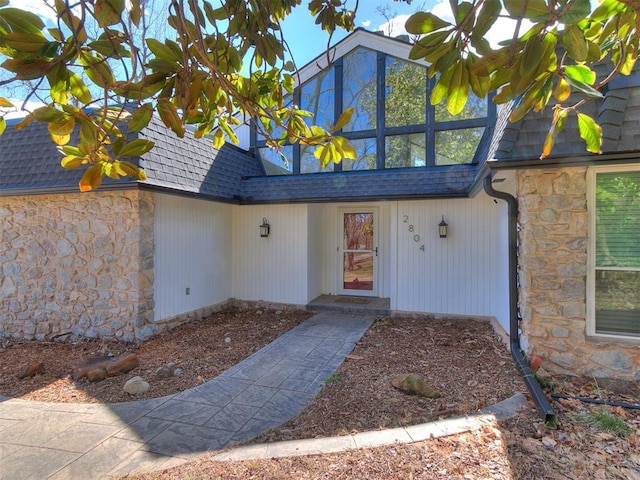 doorway to property featuring stone siding and roof with shingles