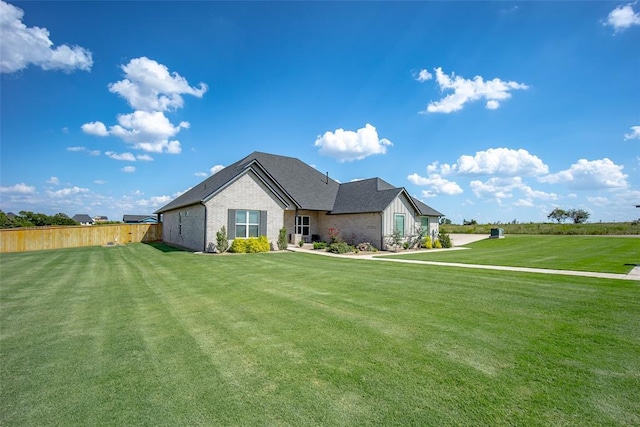 view of front of house featuring a front yard, brick siding, fence, and roof with shingles