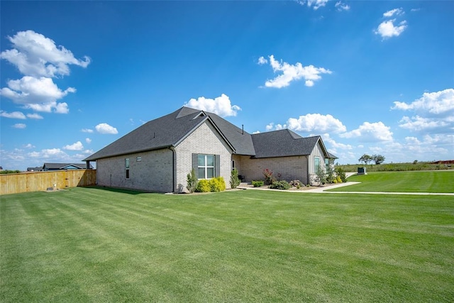 view of side of home with a yard, brick siding, and fence