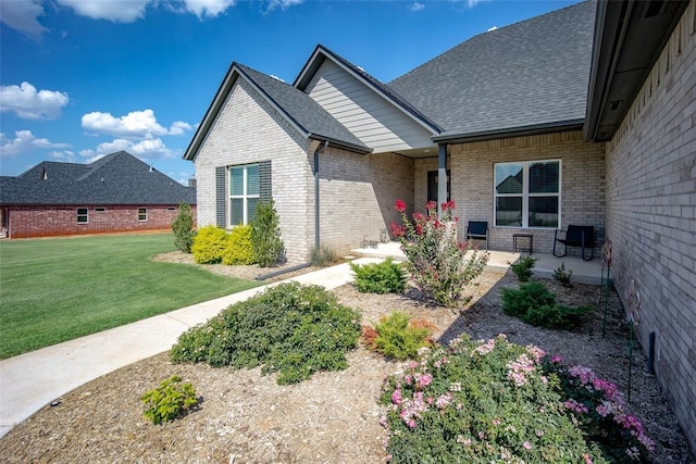 view of front facade featuring a shingled roof, a front yard, and brick siding