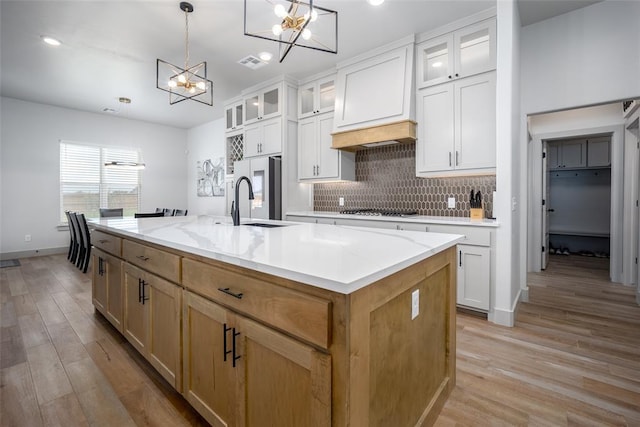 kitchen with light wood-style floors, black cooktop, a center island with sink, and backsplash