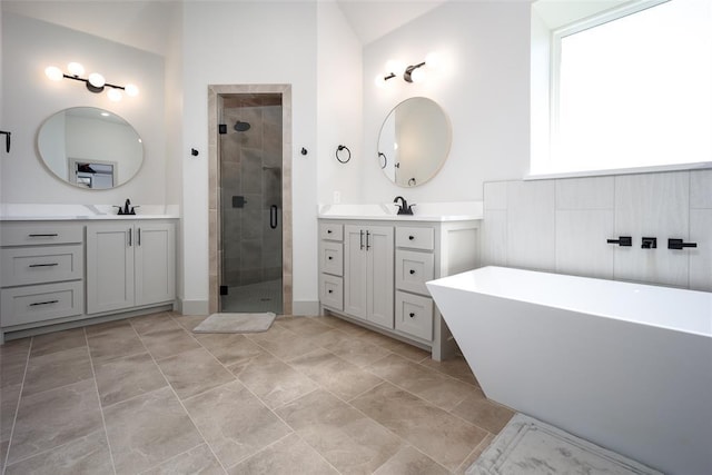 full bath featuring two vanities, a stall shower, a soaking tub, and a sink