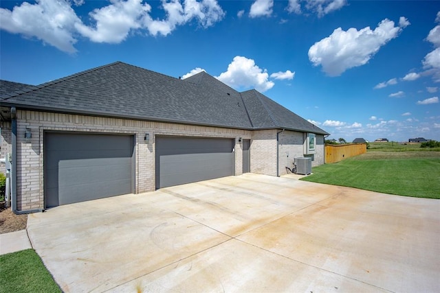 view of side of property featuring a yard, a shingled roof, central AC unit, a garage, and driveway