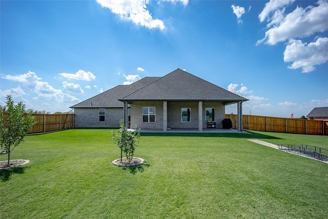 back of property with brick siding, roof with shingles, a lawn, a patio area, and a fenced backyard