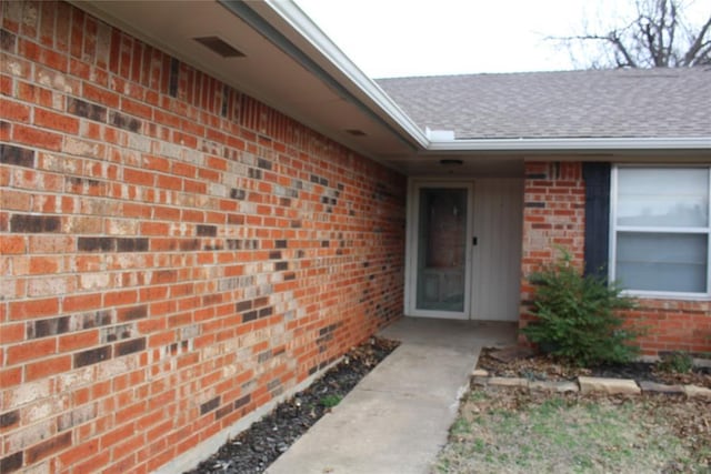 doorway to property featuring roof with shingles, visible vents, and brick siding