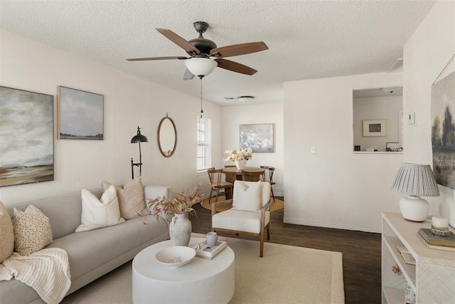 living area with a textured ceiling, dark wood-style flooring, a ceiling fan, and baseboards