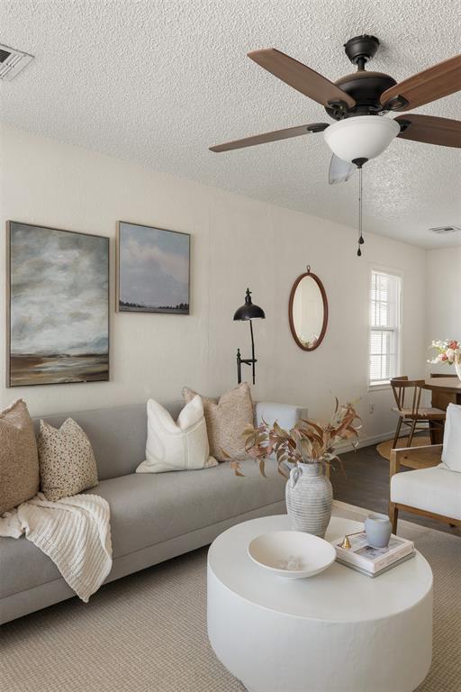 living area with a ceiling fan, visible vents, and a textured ceiling