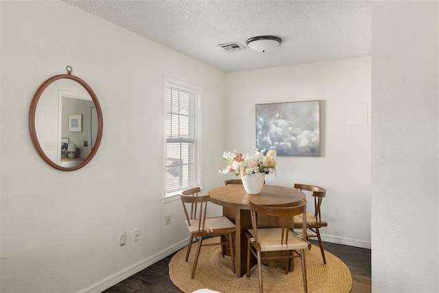 dining space featuring dark wood-style floors, visible vents, baseboards, and a textured ceiling