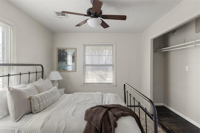 bedroom featuring a textured ceiling, wood finished floors, visible vents, baseboards, and a closet