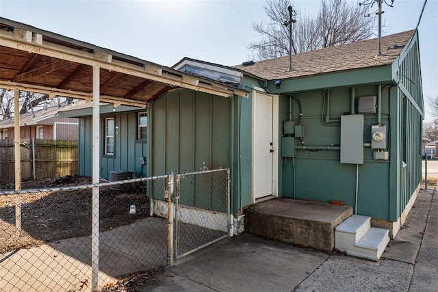 view of side of home featuring a shingled roof, board and batten siding, fence, and a gate