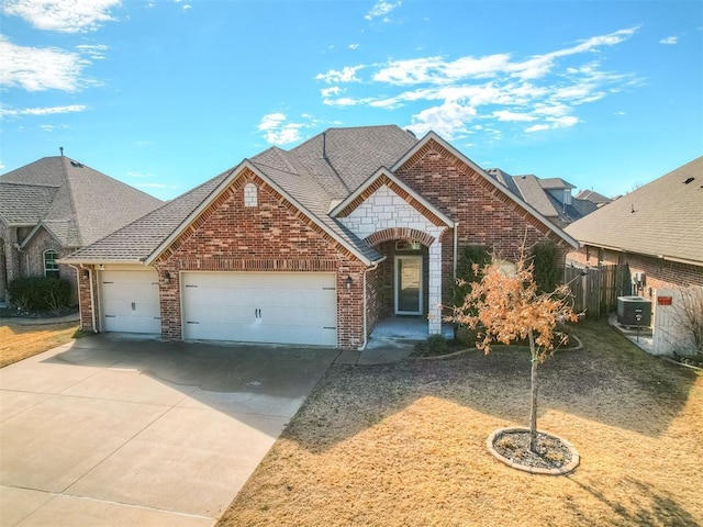 french country home with a garage, concrete driveway, brick siding, and central AC