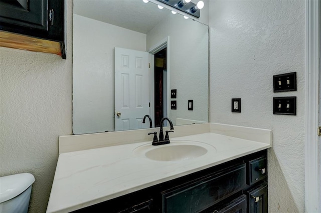 bathroom featuring toilet, vanity, and a textured wall