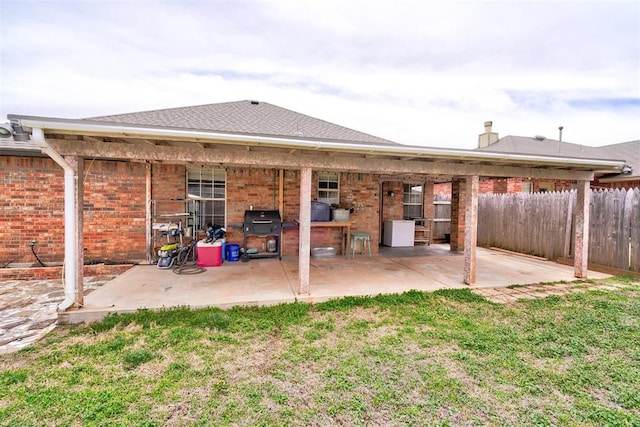 back of property featuring a lawn, a patio, fence, a shingled roof, and brick siding