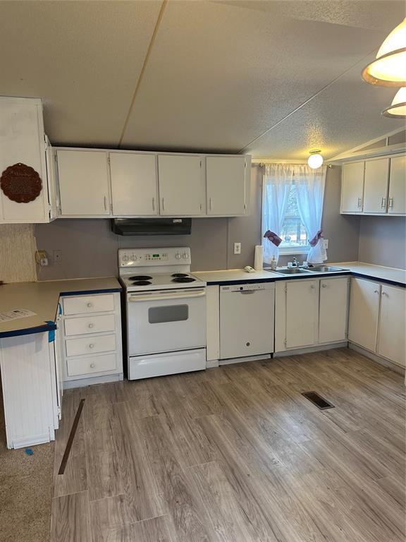 kitchen with under cabinet range hood, white appliances, a sink, white cabinetry, and light wood finished floors