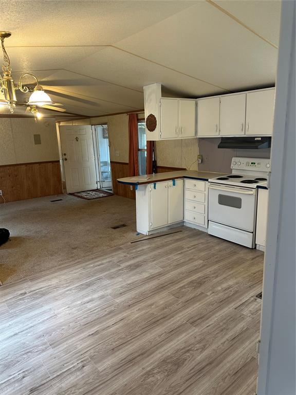 kitchen featuring white range with electric stovetop, open floor plan, wainscoting, vaulted ceiling, and under cabinet range hood