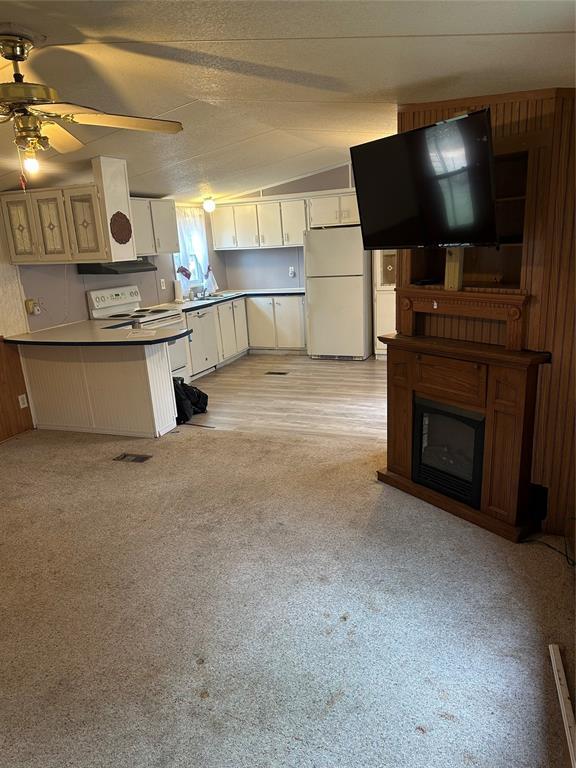 kitchen featuring a ceiling fan, a glass covered fireplace, white cabinets, white appliances, and a peninsula