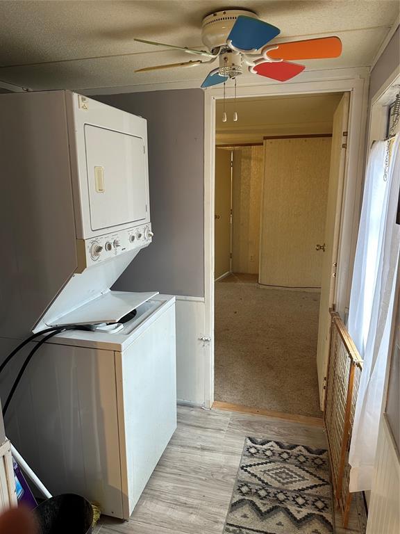 laundry area with laundry area, ceiling fan, light wood-style floors, and stacked washer / drying machine