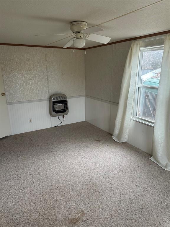 spare room with carpet, heating unit, ornamental molding, wainscoting, and ceiling fan