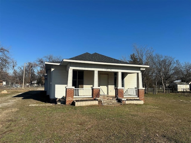 rear view of property with a yard, a porch, roof with shingles, and brick siding