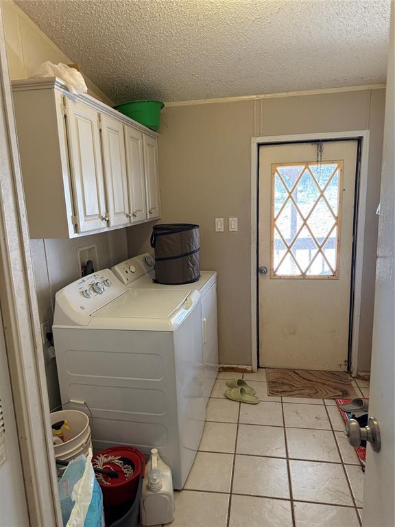 washroom featuring a textured ceiling, washer and clothes dryer, light tile patterned flooring, and cabinet space