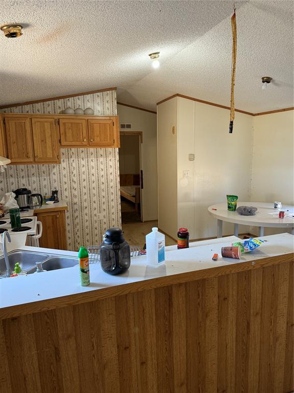 kitchen featuring visible vents, lofted ceiling, brown cabinets, light countertops, and a textured ceiling