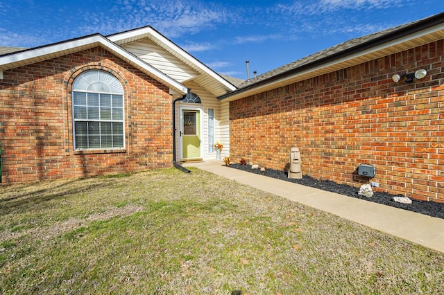 doorway to property with brick siding and a yard