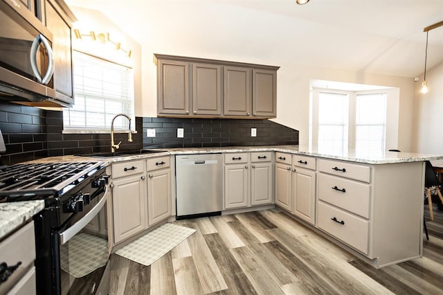 kitchen with light wood finished floors, lofted ceiling, appliances with stainless steel finishes, a sink, and a peninsula