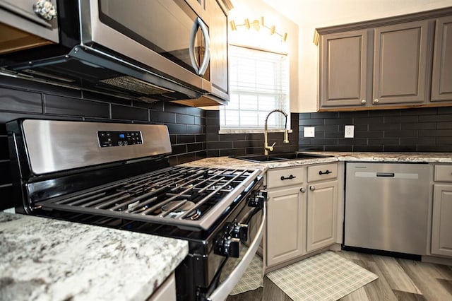 kitchen with appliances with stainless steel finishes, light wood-type flooring, a sink, and decorative backsplash