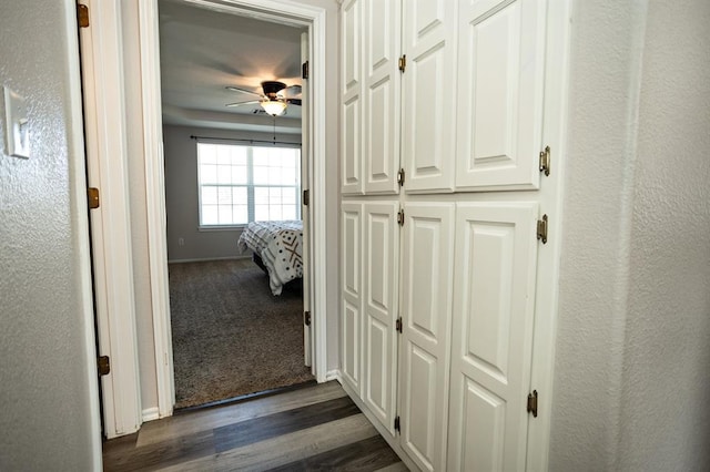 hall featuring dark wood-type flooring, a textured wall, and baseboards