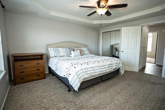 bedroom with a closet, carpet flooring, a raised ceiling, and a ceiling fan