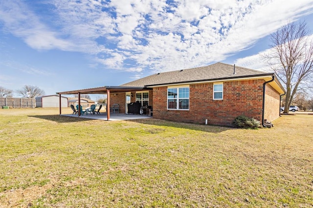 rear view of house with a patio, brick siding, fence, a yard, and roof with shingles