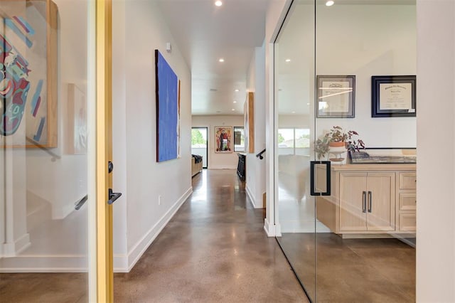 hall with finished concrete flooring, baseboards, and recessed lighting