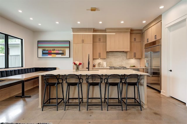 kitchen with light countertops, light brown cabinetry, a sink, concrete flooring, and stainless steel built in refrigerator