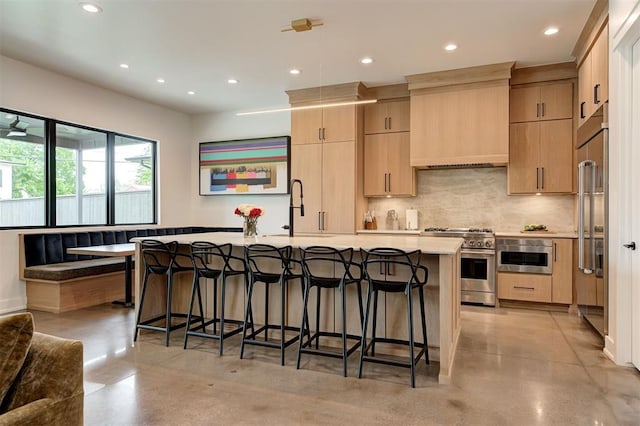 kitchen featuring high quality appliances, a breakfast bar, concrete flooring, and light brown cabinetry