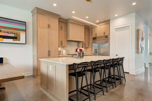 kitchen with tasteful backsplash, light brown cabinetry, stainless steel built in fridge, concrete floors, and baseboards