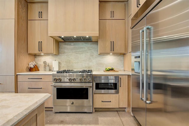 kitchen with light stone countertops, light brown cabinets, decorative backsplash, and premium appliances