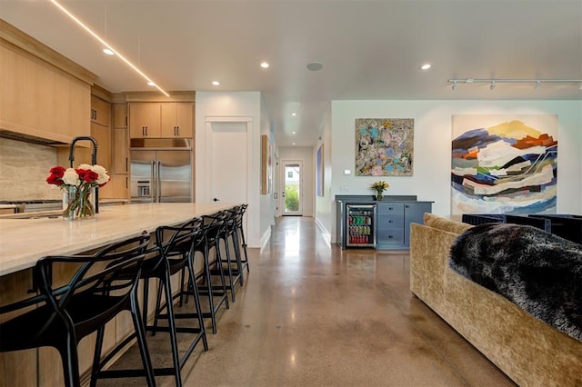 kitchen featuring beverage cooler, decorative backsplash, built in refrigerator, light countertops, and light brown cabinetry