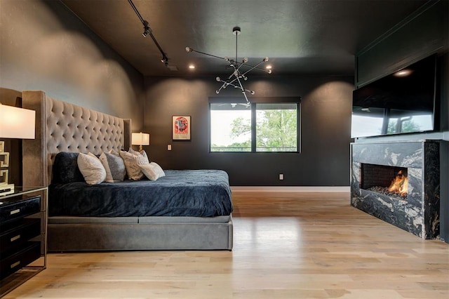 bedroom featuring light wood finished floors, a fireplace, baseboards, and rail lighting