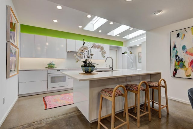 kitchen featuring finished concrete flooring, a breakfast bar area, white cabinets, a sink, and white appliances