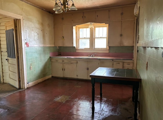 kitchen featuring tile countertops, a sink, tile walls, and a notable chandelier