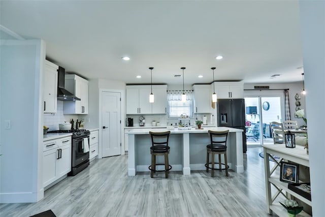 kitchen featuring wall chimney exhaust hood, white cabinetry, black appliances, a healthy amount of sunlight, and a kitchen breakfast bar