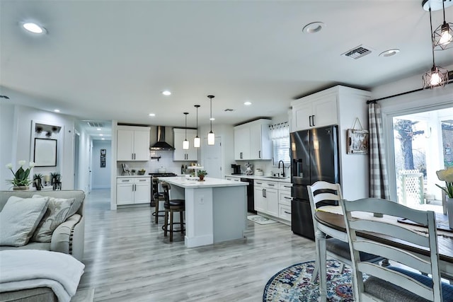 kitchen with wall chimney exhaust hood, a kitchen breakfast bar, open floor plan, stainless steel appliances, and a sink