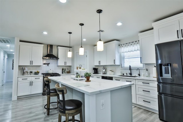 kitchen with a sink, visible vents, wall chimney range hood, stainless steel gas range, and black refrigerator with ice dispenser